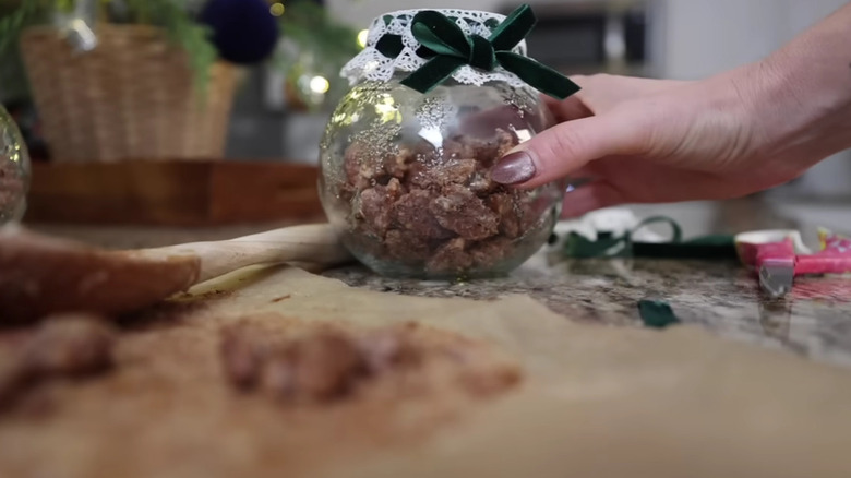 A hand holding a glass jar filled with candied nuts.