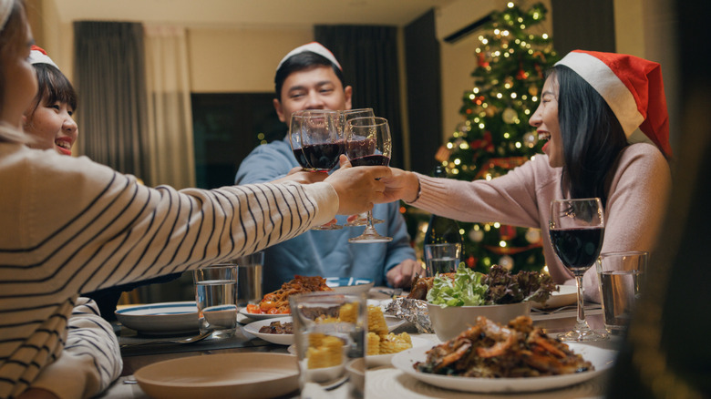 A group of people clinking red wine glasses together over a holiday dinner.