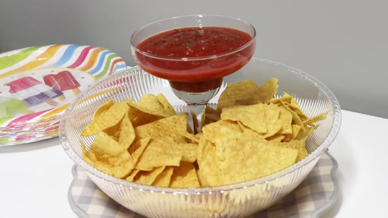 Chips and salsa served in a plastic bowl with a margarita glass filled with salsa.