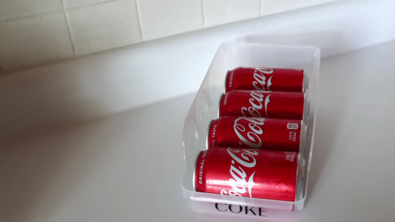 Plastic soda can organizer filled with Coca Cola cans sitting on a kitchen counter.