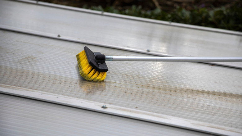 A broom cleaning a patio pergola roof cover made of aluminum.