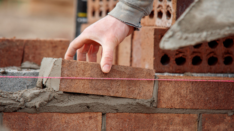 The hand of a builder, laying red bricks at a construction site.