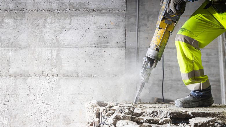 Construction worker using heavy-duty jackhammer tool and breaking reinforced concrete.