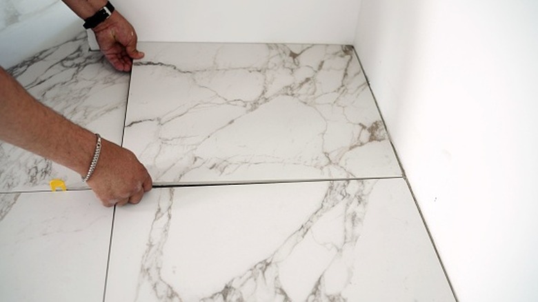 Hands placing large white porcelain tiles with marble effect into a corner.