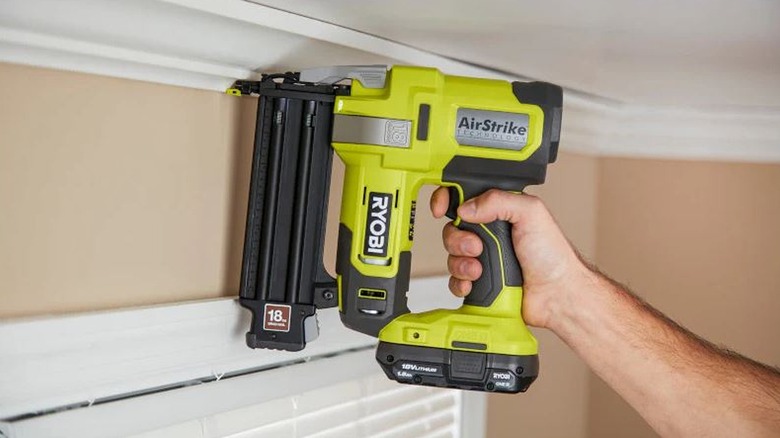 An extended hand holds the Ryobi AirStrike against the wall to nail in crown molding.