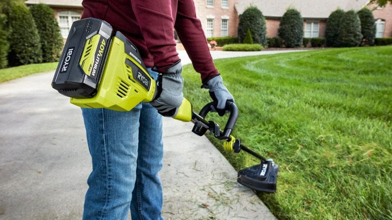 A person uses the Ryobi trimmer on lush front lawn.