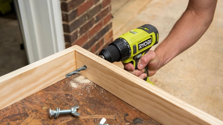 A Ryobi drill makes a hole in a wooden frame.