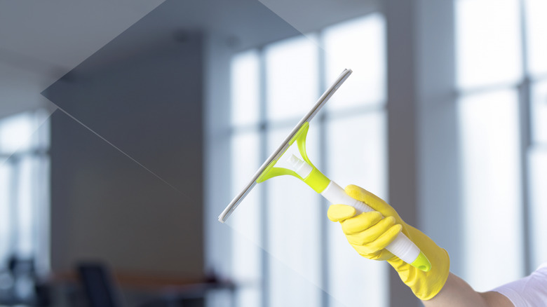 A gloved hand cleaning a glass window using a squeegee.