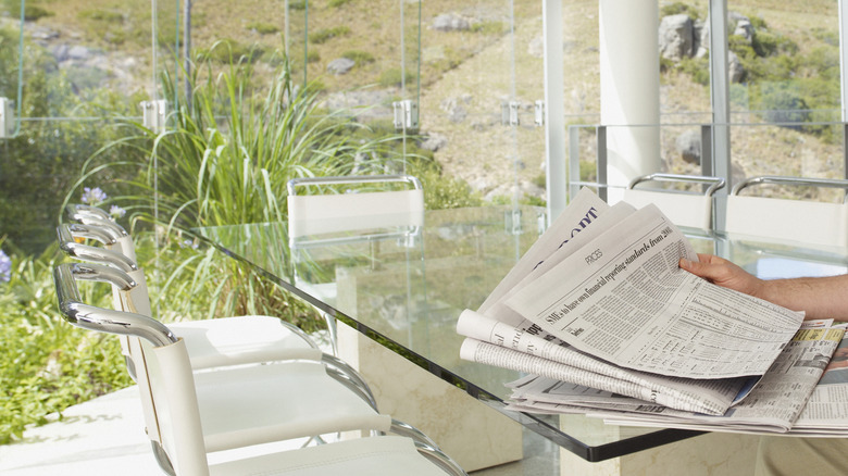 A hand holding a bundle of newspapers in front of a clean window-wall.