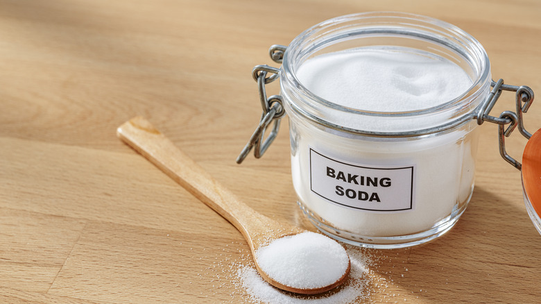 Baking soda in a glass jar and a wooden spoon.