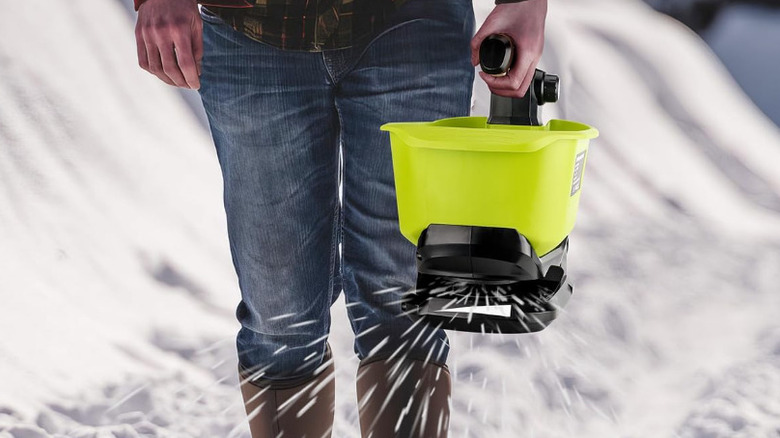 A man using a Ryobi salt spreader to disperse deicer on snow.