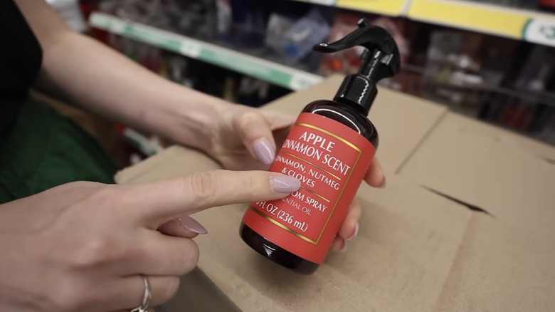 A lady with polished nails holding a bottle of apple cinnamon spray and pointing at the label