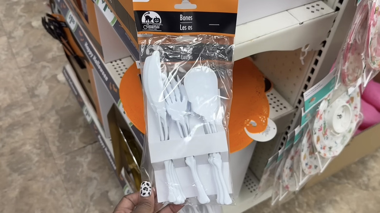 A 12-pack of white knives, forks, and spoons shaped like bones hanging from a rack in a Dollar Tree store