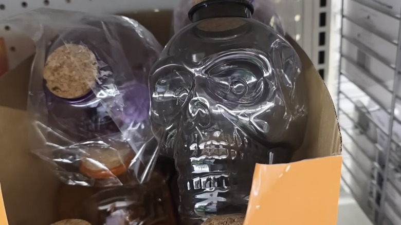 A plastic skull-shaped bottle with a cork top sitting on a shelf in a Dollar Tree store