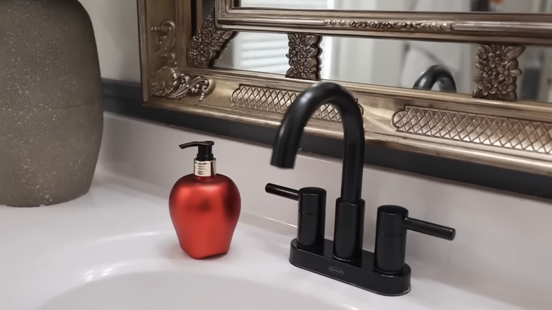 A hand soap dispenser shaped like a red apple next to a sink with a black faucet and handles