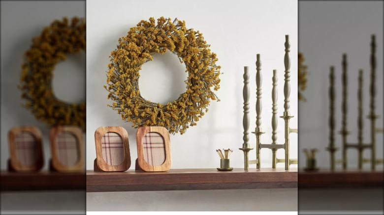 A wreath made of golden yarrow hangs over a shelf.
