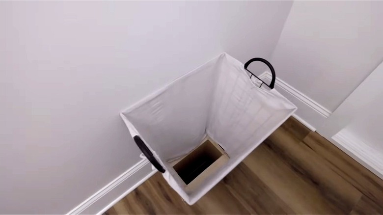 A laundry chute is hidden inside a white laundry basket.