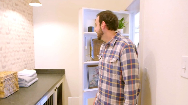 A man walks into his new laundry room which sits behind a bookshelf Murphy door on episode 3 of season 2 of HGTV show "Fixer to Fabulous"