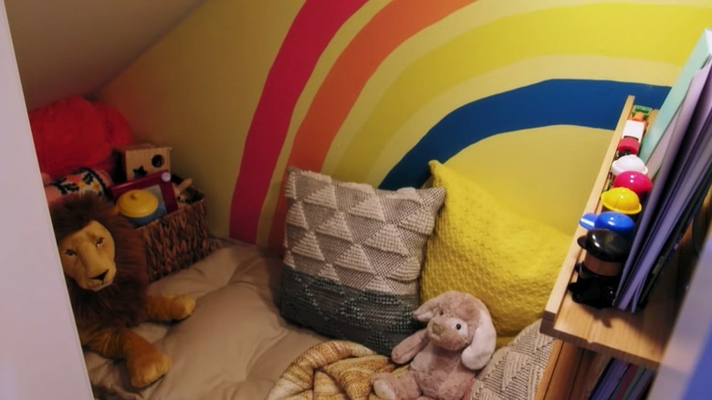 Screengrab from HGTV's "Hidden Potential" season 2, episode 11, showing a secret playroom underneath a staircase with a rainbow design on the wall and kid's toys scattered all around.