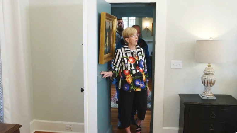 Woman walks into bedroom with white walls from the entry way. Door to the room is concealed behind blue gallery wall.
