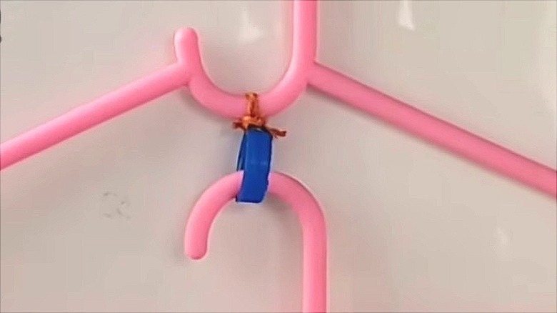 A closeup of two pink clothes hangers joined together using a plastic laundry bottle lid.