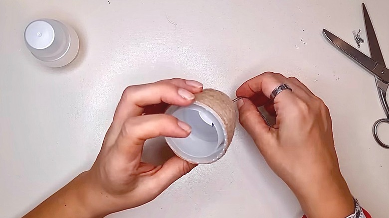 A person wraps a plastic detergent cap in twine.