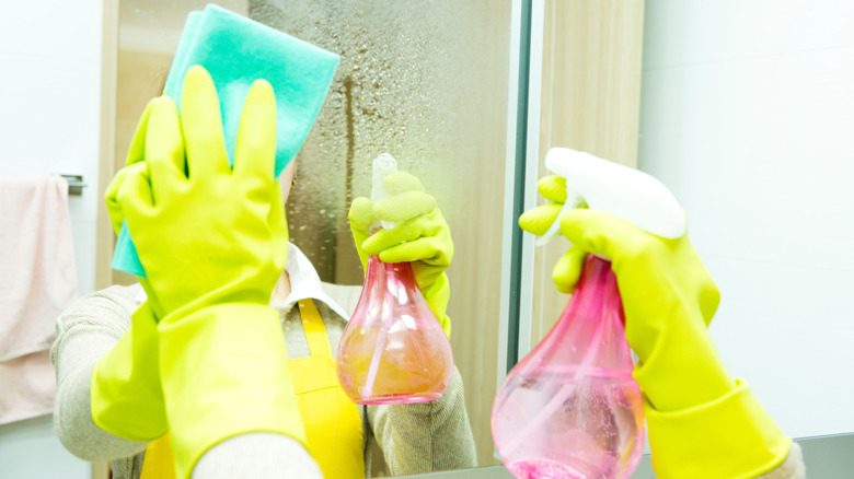 Person cleaning bathroom mirror with sponge and vinegar solution.