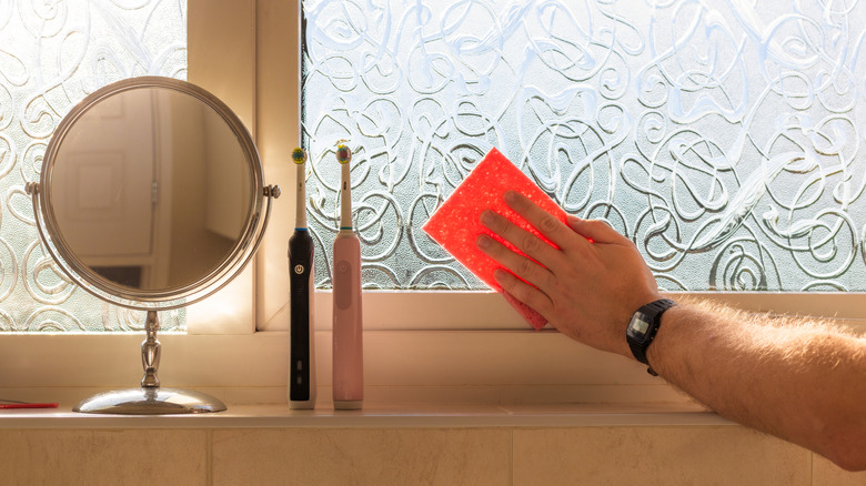 Person cleaning glass window in bathroom.