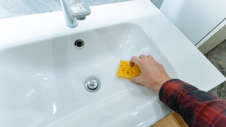 Hand cleaning bathroom sink with sponge.