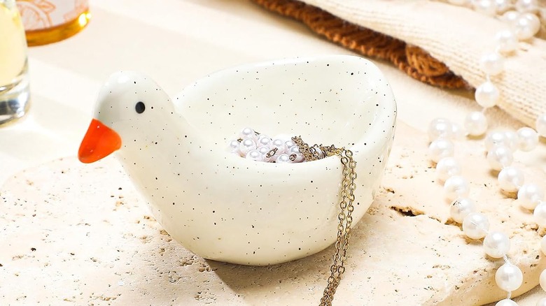A goose ring dish holding a necklace sits on a cluttered vanity countertop.