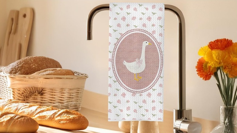 A pink and white tea towel with a goose illustration and floral print hangs on the faucet in a kitchen.