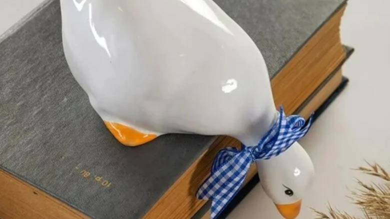 A ceramic goose with a blue gingham ribbon around its neck sits on top of a stack of books.