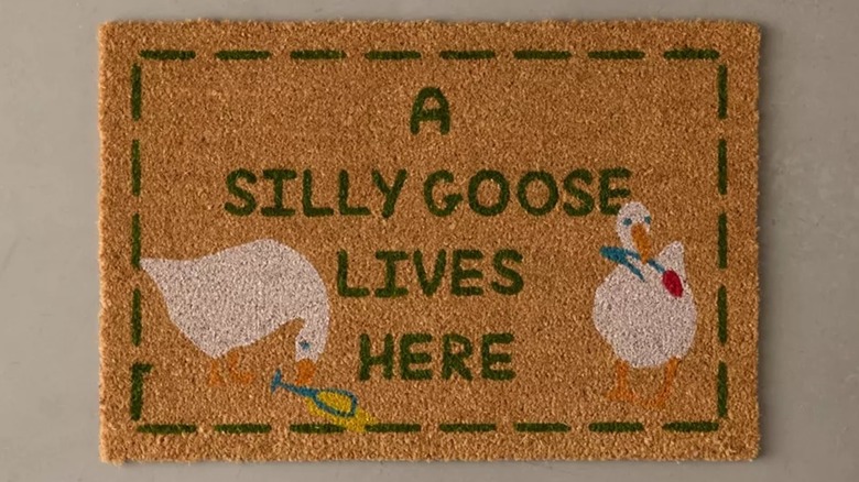 A doormat with "A Silly Goose Lives Here" text and an image of two geese holding flowers in their beaks.