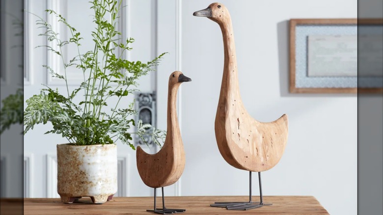 Two wooden goose sculptures on a table beside a potted houseplant in a living room.