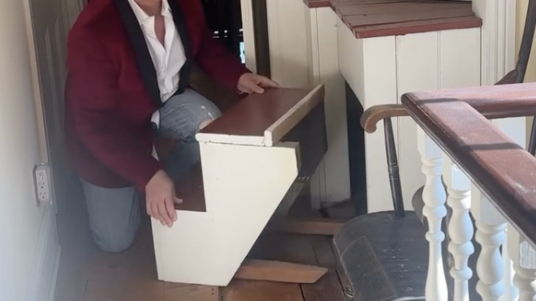 Man pulling stairs away from hidden storage in old house