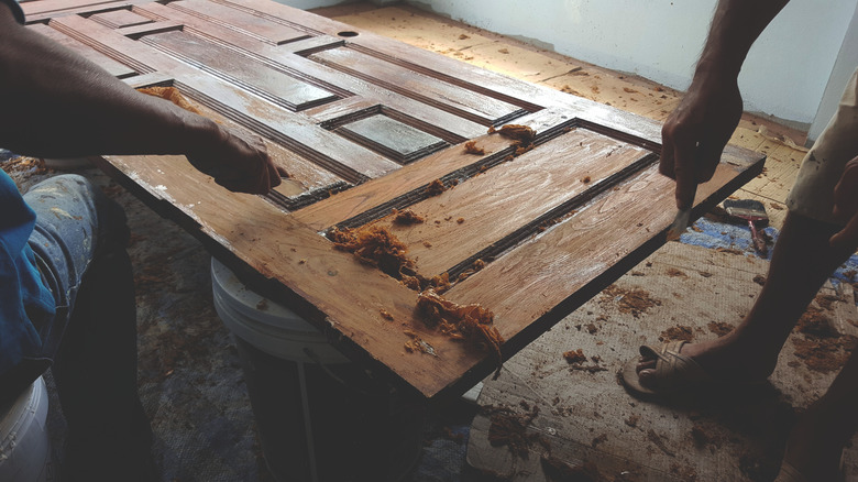 Two workers scraping paint off wood door