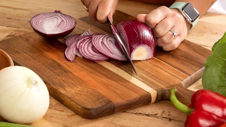 Closeup of a person's hands chopping an onion on a cutting board