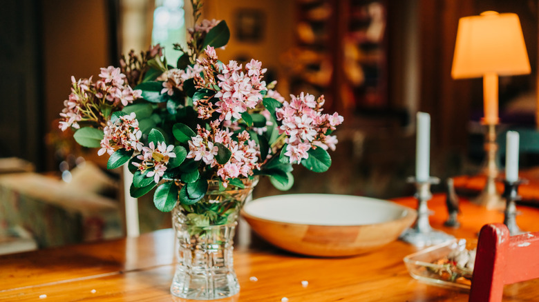 Faux flowers in a crystal vase on a wood table.