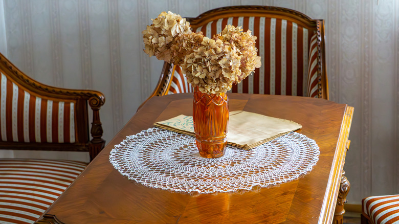 Flowers in a vase on a lace doily on a wood table