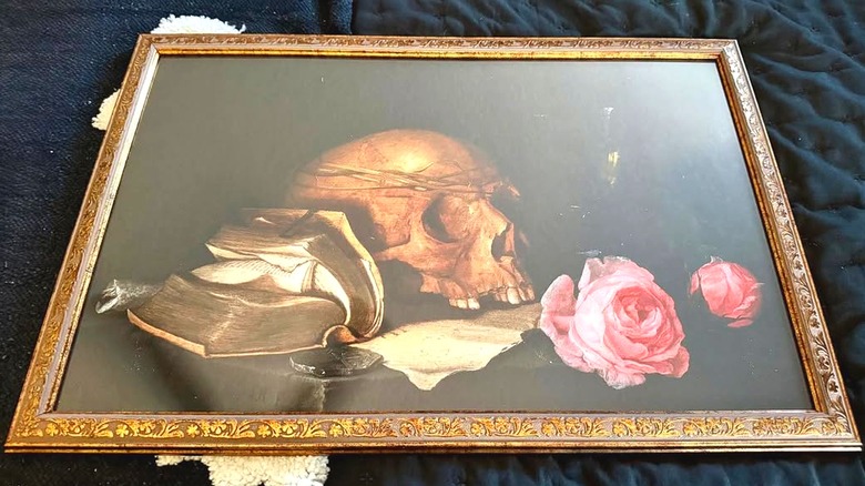 A painting of a skull, a book and two roses in a vintage frame