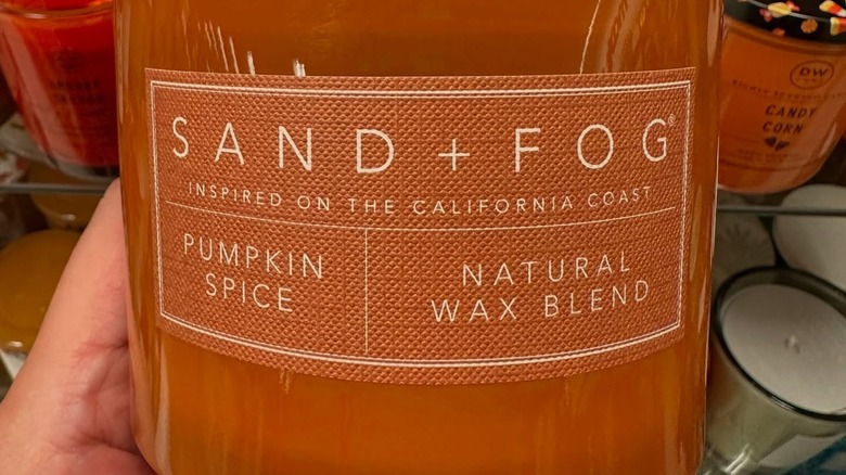 Person holds an orange pumpkin spice candle container