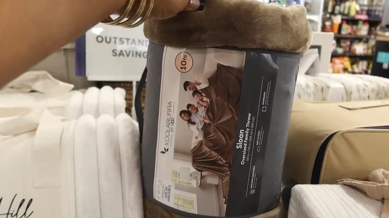 A hand holds a brown blanket displayed in a store.