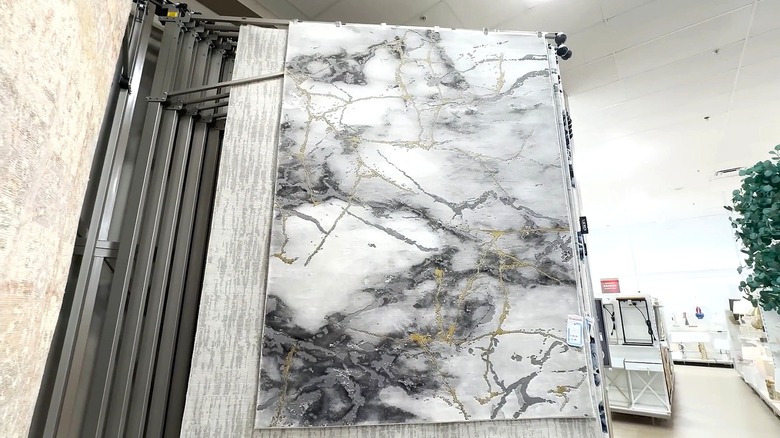 A white, grey, and gold rug is hung from a display rack at a store.