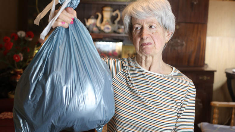 Older woman holding up a black trash bag with a frown