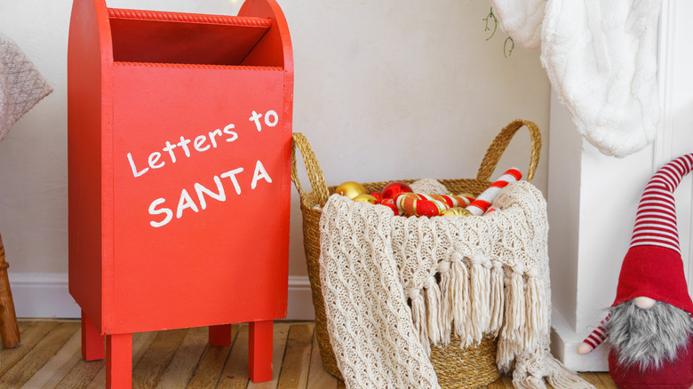 A basket filled with red, white and gold items next to a red "Letters to Santa" mailbox and a red and white gnome