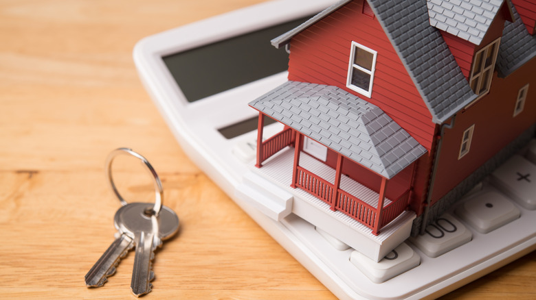 A small plastic house sits on a calculator next to a set of keys