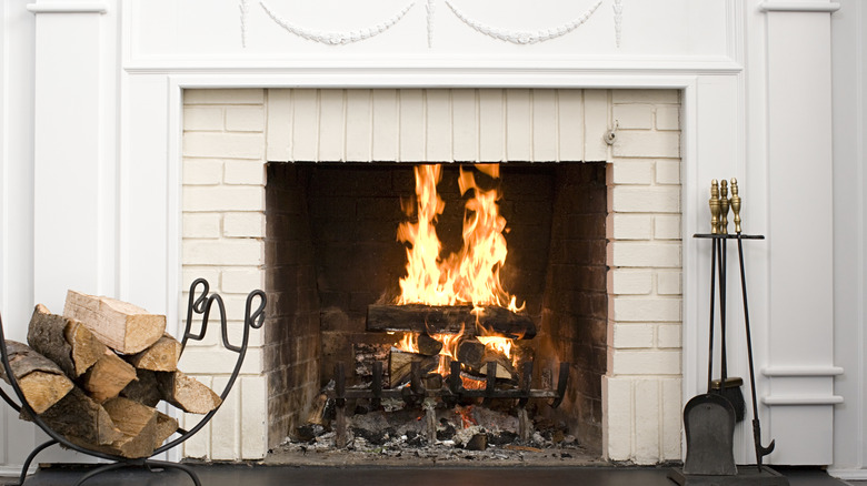 A brick fireplace, with a live fire, painted creamy white