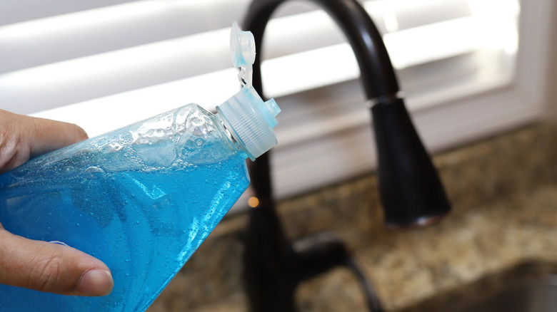 Person pouring dish soap in sink drain