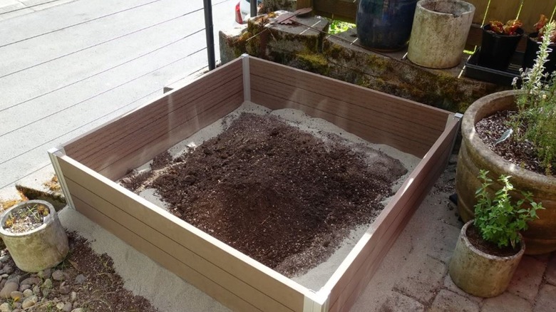 A half-filled raised garden bed made of composite decking boards.
