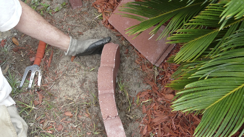 A person laying red concrete pavers to create the wall of a raised garden bed.